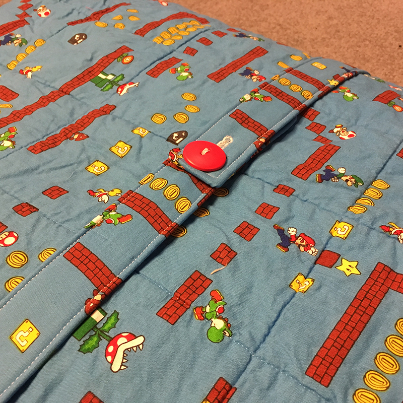 A belt made of the backing fabric is held around the quilt with a large, bright red button.