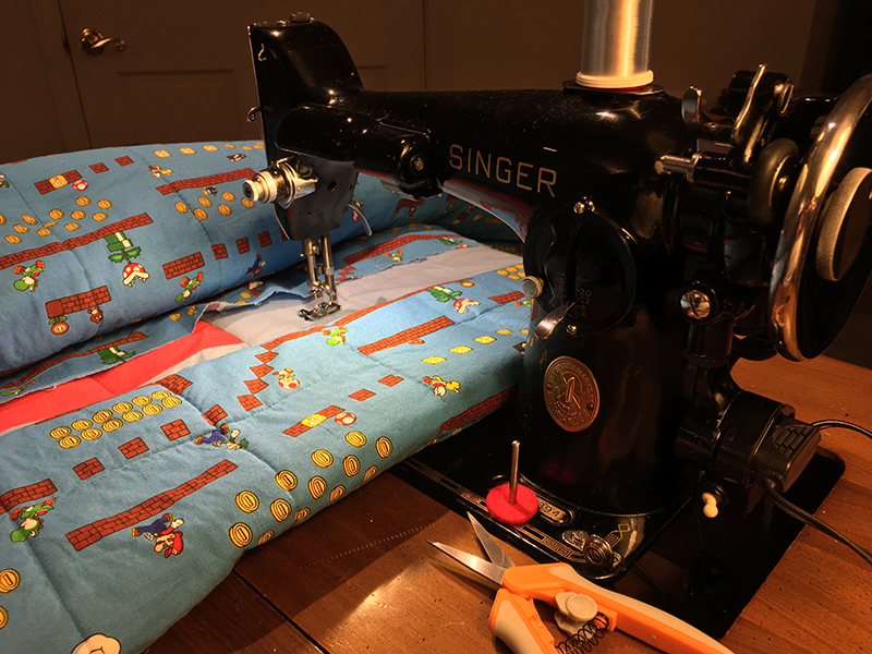 The quilt is again ready to receive a line of stitching. A spool of inviisible thread is sitting on the machine's spool pin.